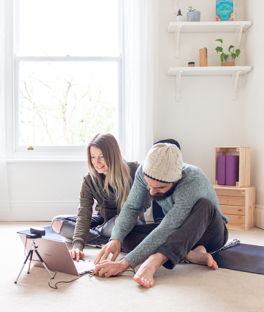Deux jeunes professeurs de yoga assis sur un tapis de yoga, devant un ordinateur avec une webcam