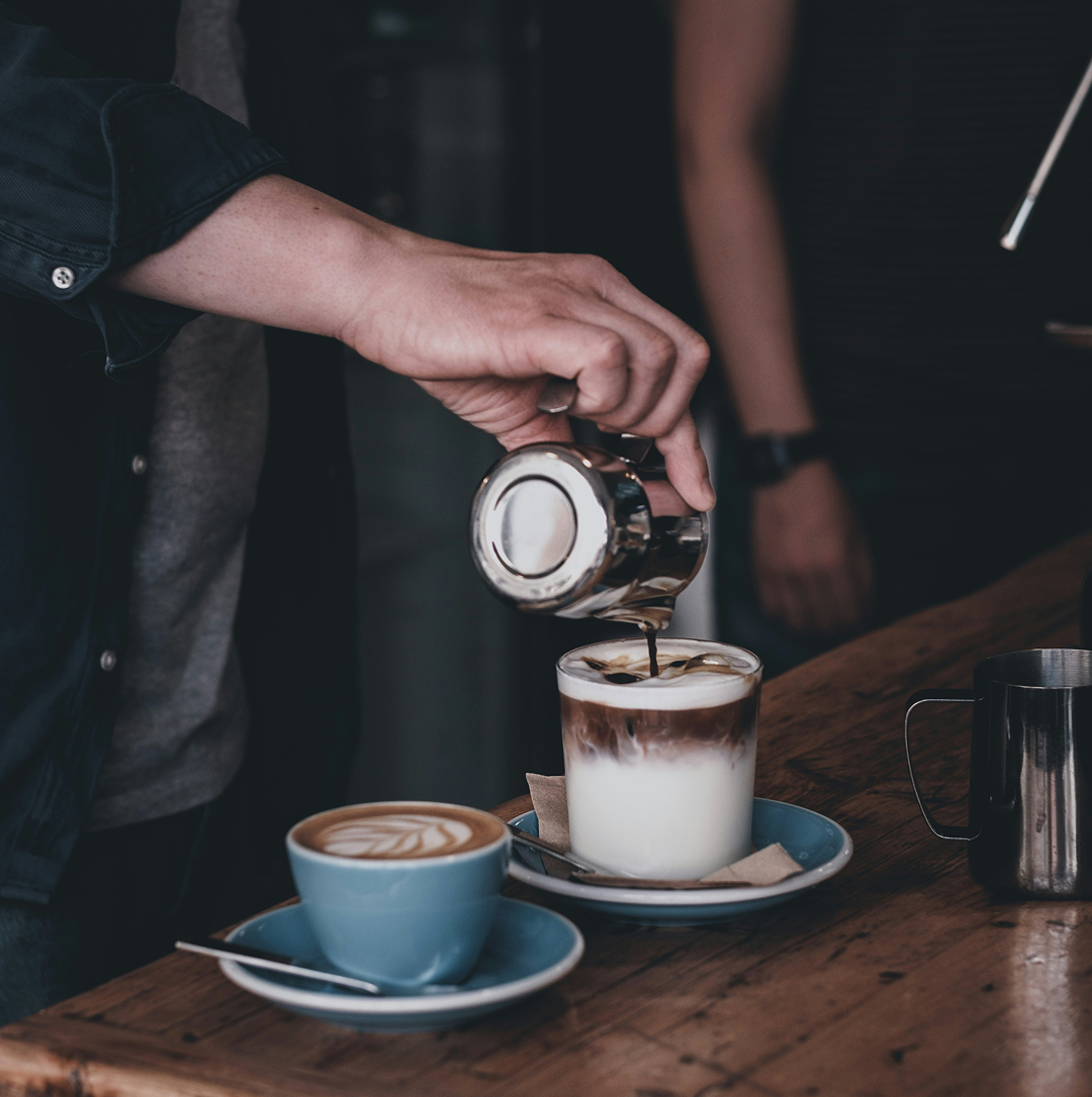Un barista verse un café glacé dans un verre, à côté d'une tasse de café chaud