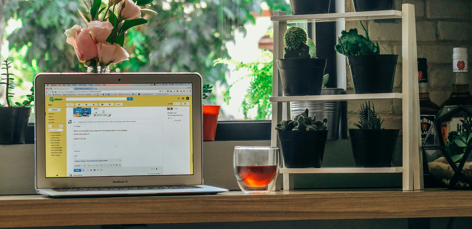 Un ordinateur sur un bureau, avec un verre de café sur le côté et des plantes